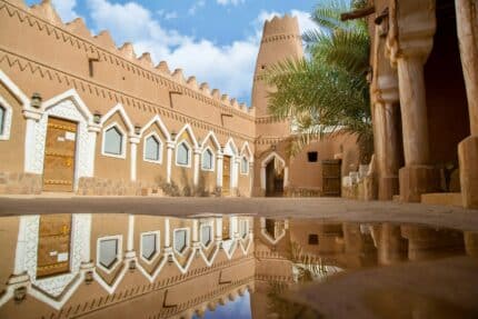 Traditional mud brick architecture with a tall tower reflected in a ground puddl