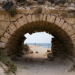 a stone tunnel on a sandy beach with the ocean in the background