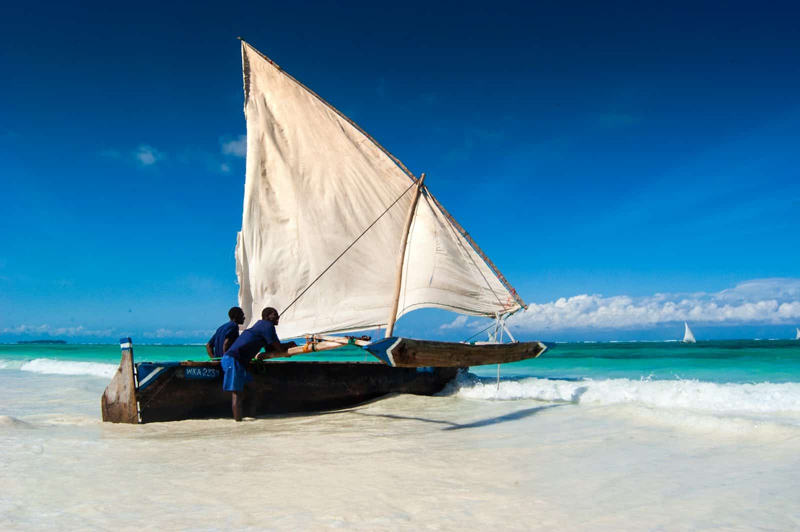 man in black shirt sitting on white and brown sail boat on sea shore during dayt
